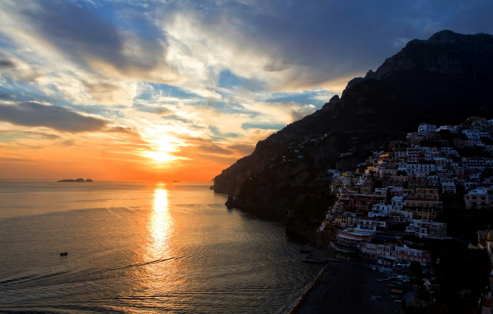 Positano's pastel cliffside houses bathed in golden light as the sun sets over the Tyrrhenian Sea